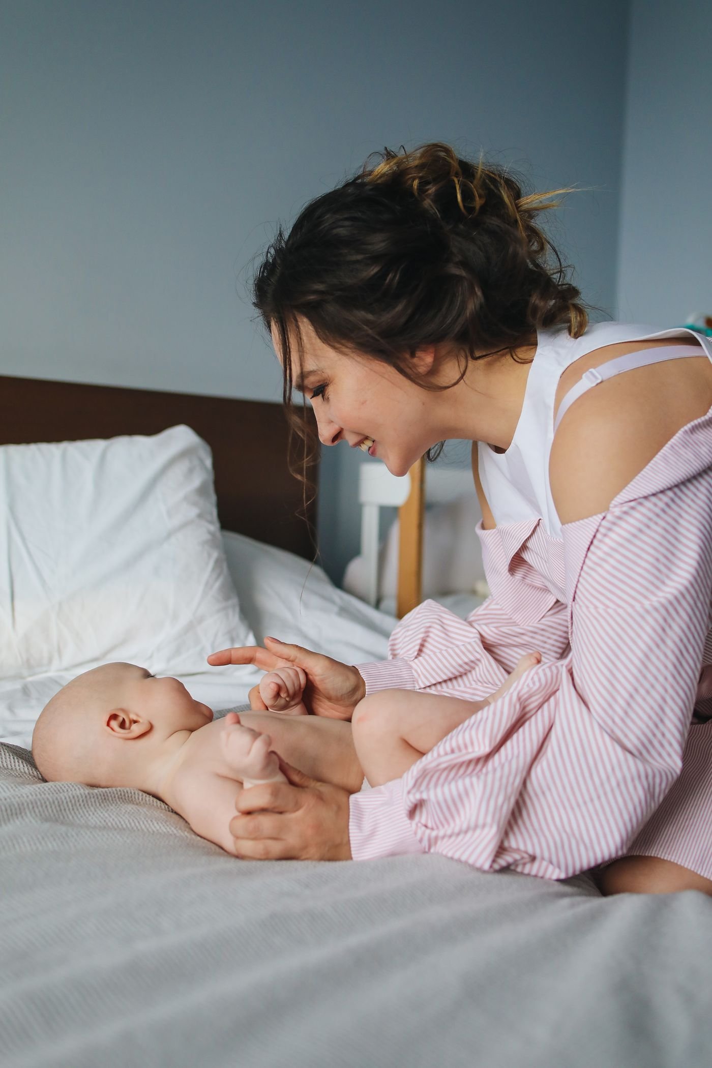 Mãe sorrindo e brincando com seu bebê, sob supervisão, sobre a cama